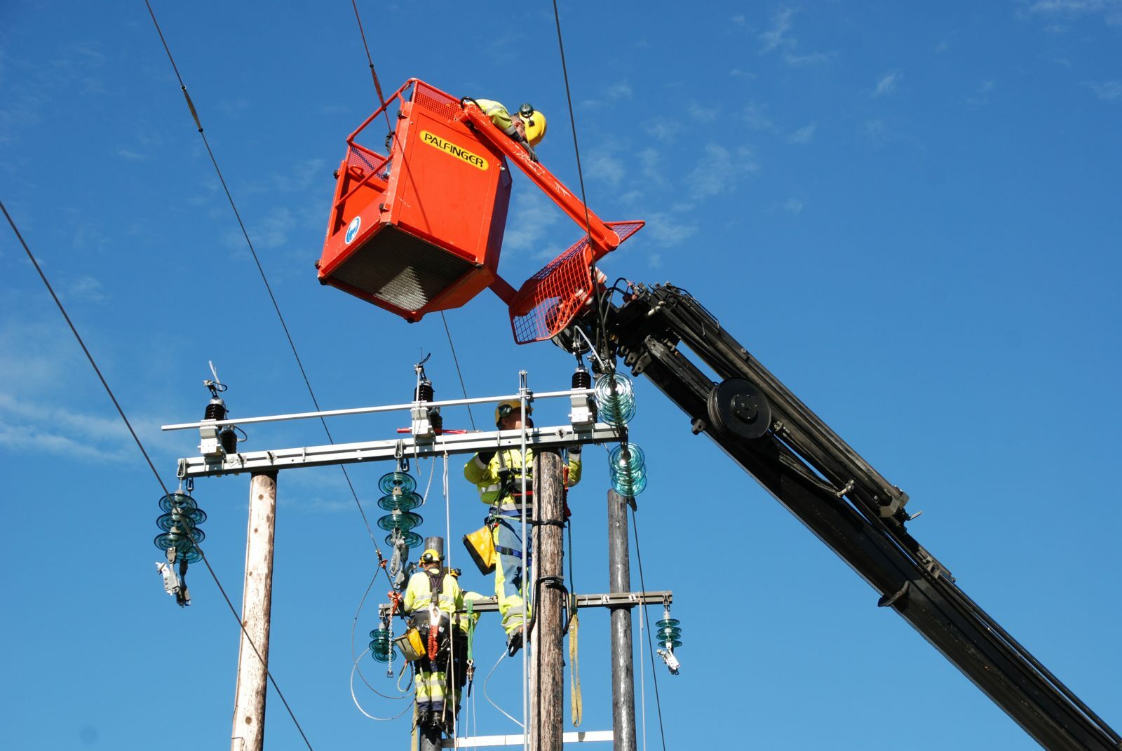 To elektriker i arbeid på strømnett linje stolpe, men den tredje er over dem i en heisekran
