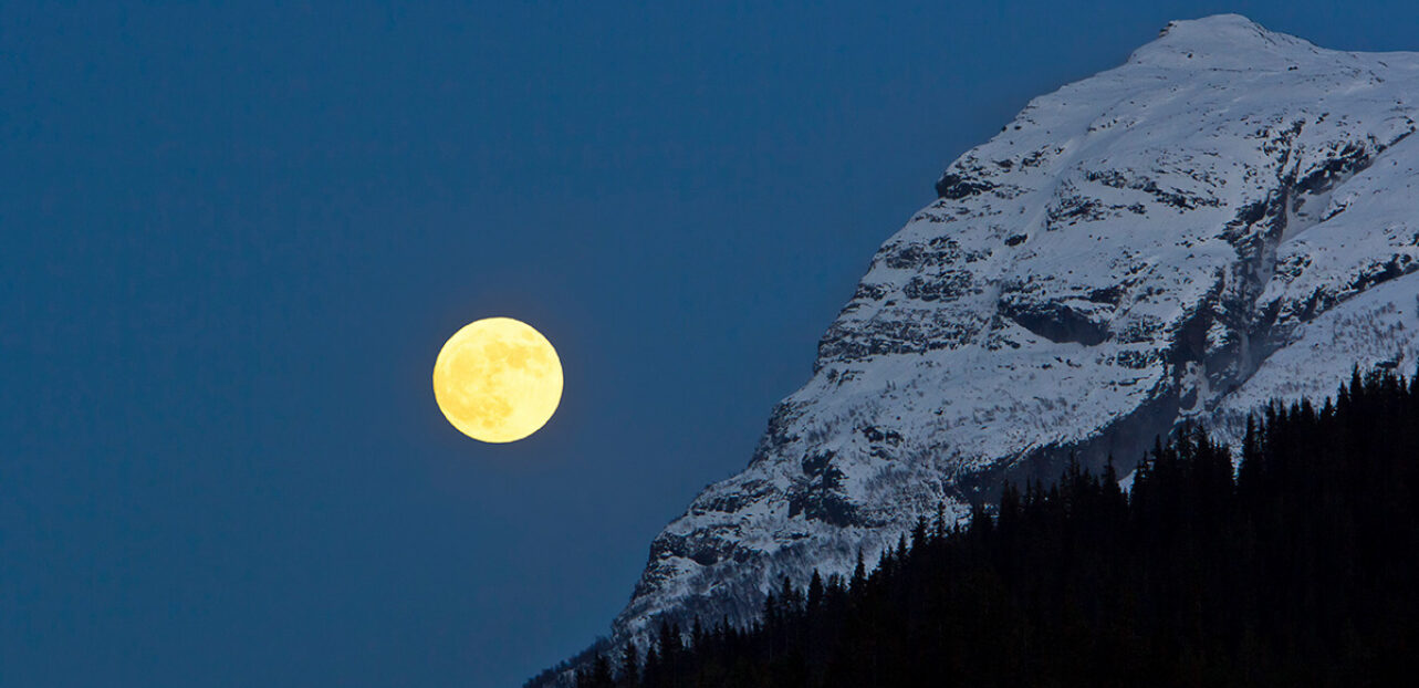 Klar nattehimmel med en skinnende fullmåne og snøfjell